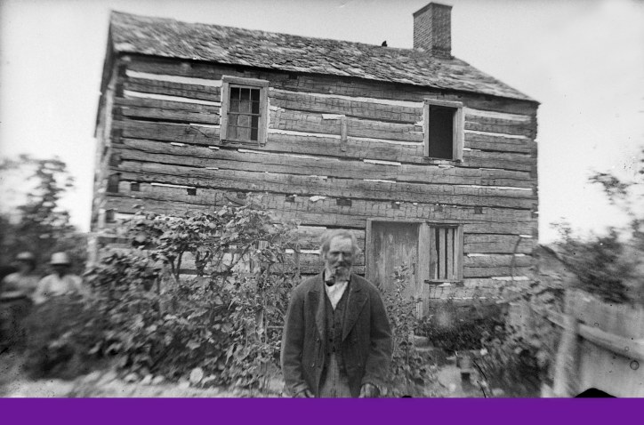 Conrad Stroh standing in front of Captain Thomas Smith's Log House.
